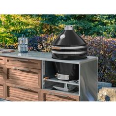 an outdoor bbq grill on top of a wooden cabinet in front of some bushes