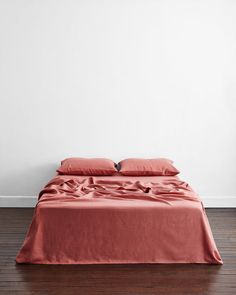 a bed with red sheets and pillows in a white room next to a wooden floor