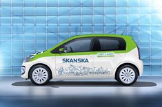 a small green and white car parked in front of a blue building with the words skanska on it