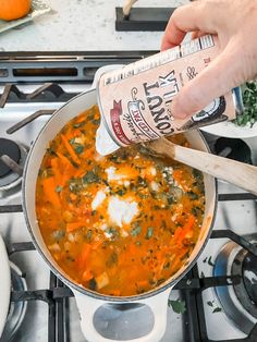 someone is adding seasoning to a pot of soup on the stove top with carrots and spinach