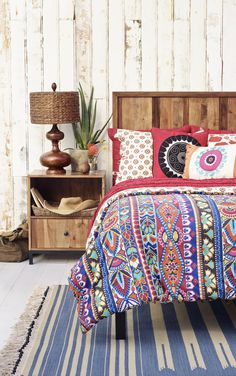 a bed with colorful pillows and blankets on top of it next to a wooden headboard