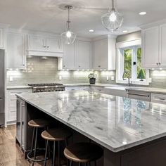 a large kitchen with marble counter tops and white cabinets, along with two stools