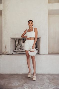 a woman standing in front of a fireplace with her hand on her hip, wearing white