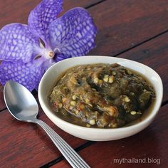 a white bowl filled with food next to a purple flower on top of a wooden table