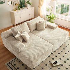 a large white couch sitting on top of a wooden floor next to a lamp and window