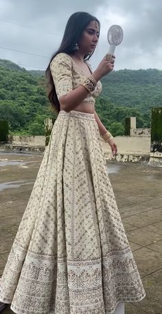 a woman in a long dress holding a fan and looking at the ground with mountains in the background