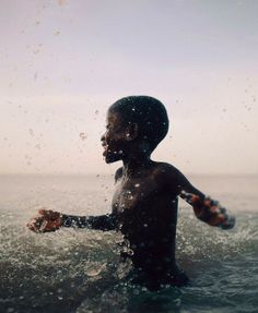 a young boy standing in the ocean with his arms outstretched