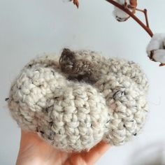 a hand holding up a crocheted object in front of a branch with cotton flowers