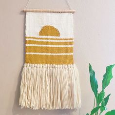 a woven wall hanging with tassels and a potted plant next to it