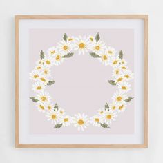 a cross stitch pattern with daisies and leaves in a wooden frame on a wall