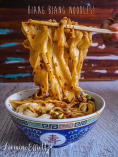 someone is holding chopsticks over noodles in a blue and white bowl on a wooden table