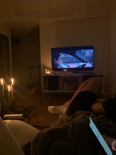 a person laying on a bed in front of a flat screen tv with candles lit