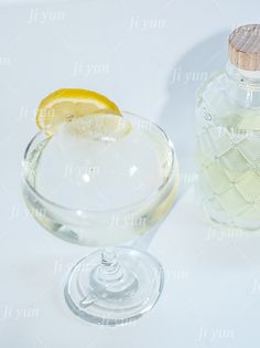 a glass filled with liquid and a lemon slice on the rim next to a bottle