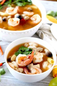 two bowls of soup with shrimp, carrots and cilantro on the side