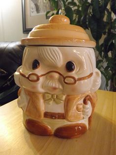 a ceramic jar with a mustache and glasses on the lid sitting on a table next to a potted plant