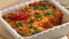 a casserole dish with tomatoes, cheese and parsley in it on a wooden cutting board