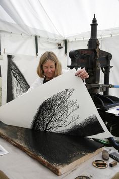 a woman holding up a piece of art with trees on it