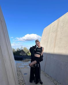 a woman posing for a photo in front of a wall with her legs crossed and one leg bent