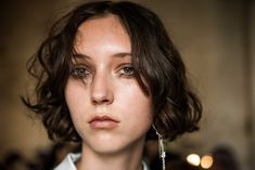 a woman with short hair wearing earrings and a white shirt is looking at the camera