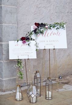 two signs with flowers and greenery on them are sitting in front of a brick wall