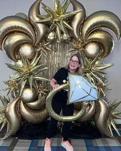 a woman standing in front of a giant golden balloon arch with a kite on it