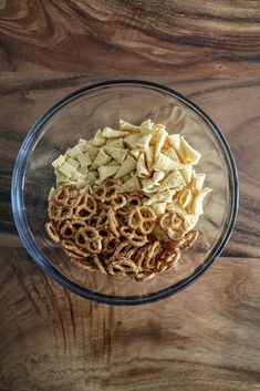 a glass bowl filled with cereal and pretzels on top of a wooden table