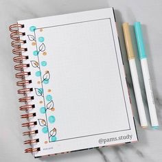 an open notebook with two pens next to it on a white surface, which is decorated with blue and orange flowers