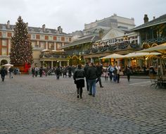 people are walking around an outdoor shopping area with christmas decorations on the trees and buildings in the background