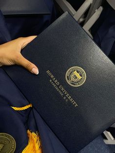 a person is holding a black book in their hand and wearing a yellow tassel