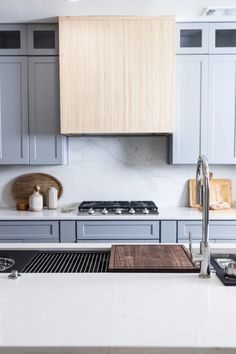 a kitchen with white counter tops and gray cupboards next to a stove top oven