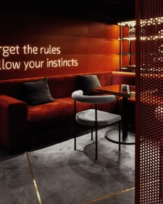 a red couch sitting next to a table in a living room under a neon sign