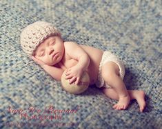 a newborn baby wearing a crochet hat and holding a baseball on a blue blanket