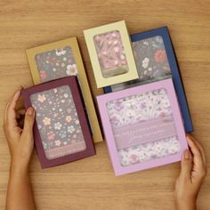 three cards with flowers are being held by someone's hands on a wooden table