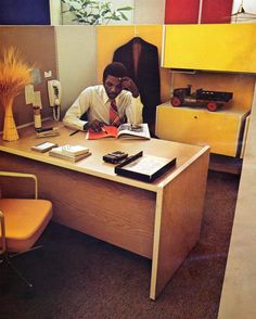 a man sitting at a desk in front of a yellow cabinet with a phone on it