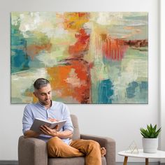 a man sitting on a couch reading a book in front of a large abstract painting