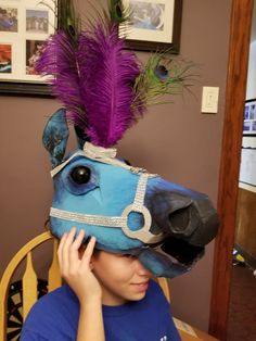 a woman sitting at a table with a horse mask on her head and purple feathers sticking out of it