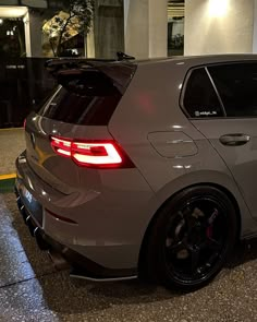 the rear end of a silver car parked in a parking lot next to a building