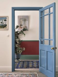 an open door leading into a room with a potted plant on the floor and paintings on the wall