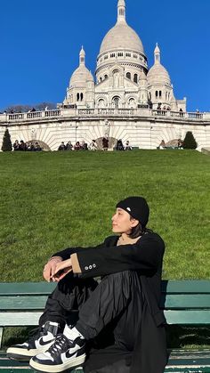 a man sitting on top of a green bench in front of a large white building