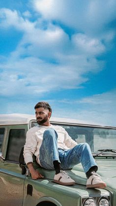 a man sitting on the hood of a green truck in front of a blue sky