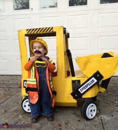 a little boy that is standing in front of a construction truck with a fake moustache on his face