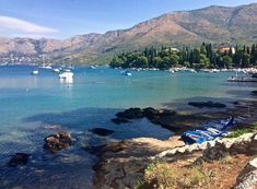 there are many boats in the water at this beach near some hills and trees on the shore