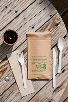 a table topped with white utensils and a brown bag next to a cup