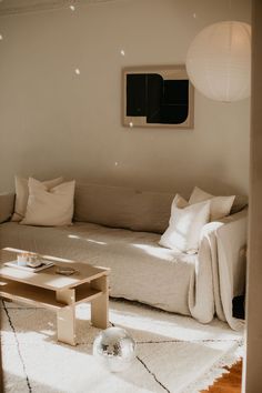 a living room with a white couch and coffee table in the corner, light coming through