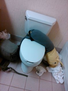 a toilet that is in a bathroom next to a trash can and some paper on the floor