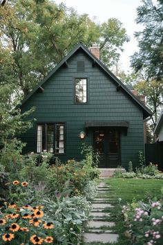 a green house with lots of flowers in the front yard and walkway leading up to it