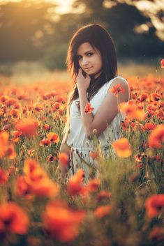 a woman standing in a field of flowers with her hand to her face and looking at the camera