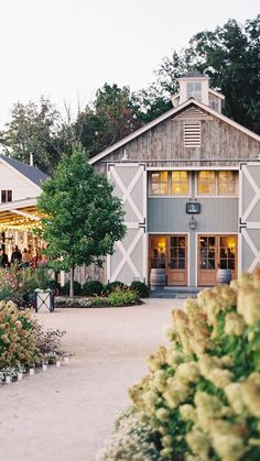 an old barn is surrounded by flowers and greenery in front of the building at dusk