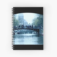 people standing on a bridge over a river in front of a building with a clock tower spiral notebook