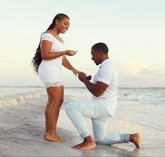 a man kneeling down next to a woman on the beach